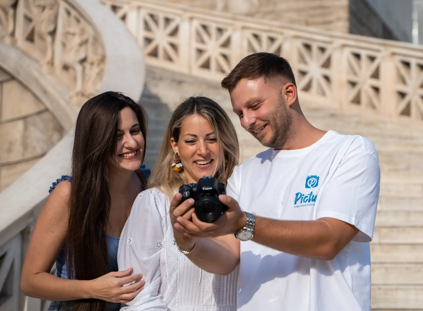 A photographer is showing a set of photos on the camera display to two women, who are closely inspecting the images with interested expressions.